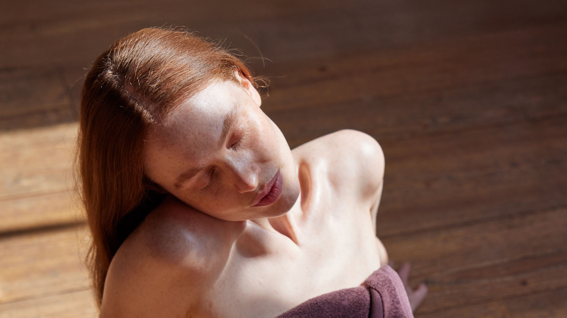 Frau im Handtuch eingewickelt sitzend auf einem natürlichen Holzuntergrund genießt die Sonne