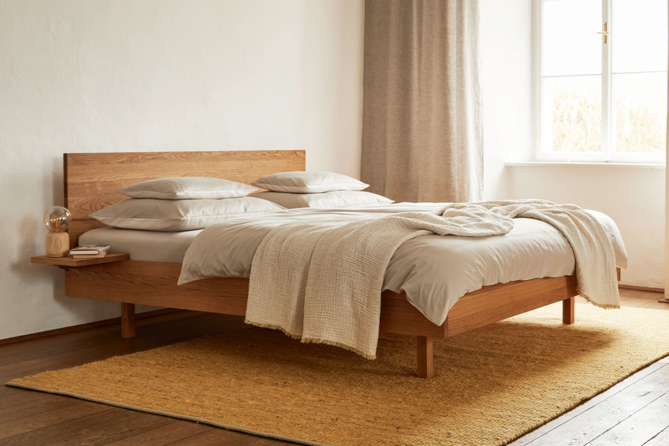 Holzbett mit grauer Bettwäsche in einem Schlafzimmer