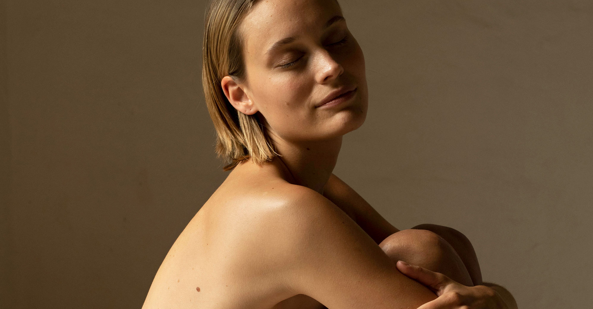 Frau sitzt mit verschränkten Armen und geschlossenen Augen vor neutralem Hintergrund