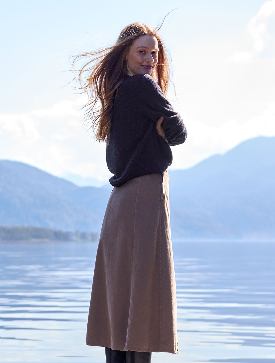 Frau steht am See und trägt braunen Rock