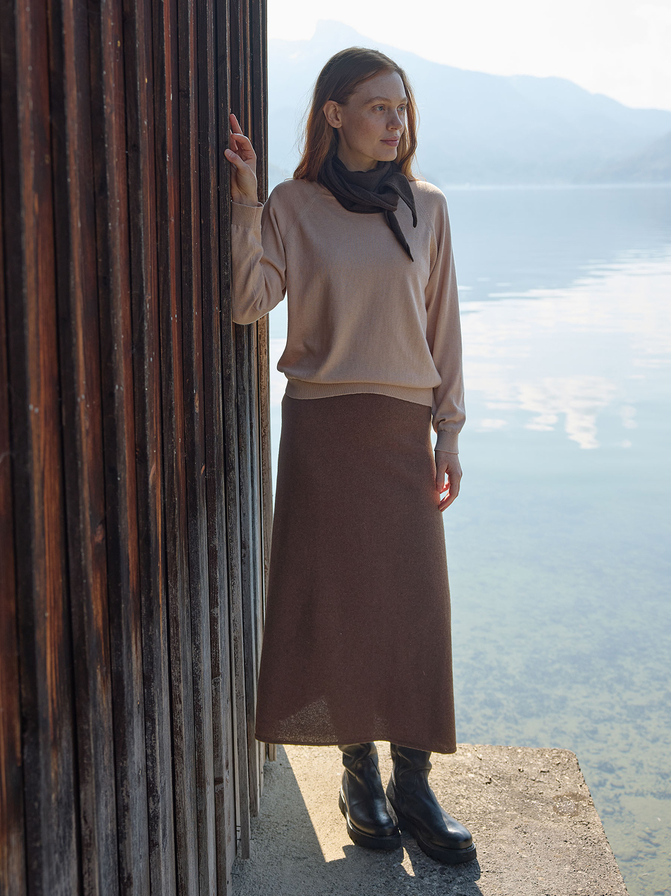 Frau steht am See und trägt braunen Rock