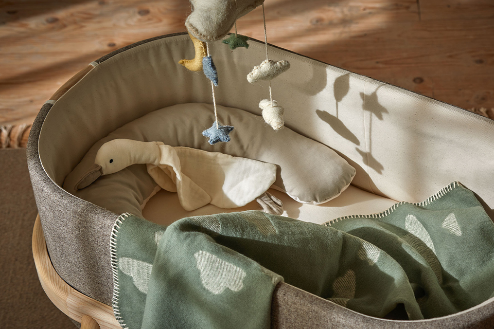 Graue Babywiege mit Kuschelgans und einer Kuscheldecke mit Wolkenmuster