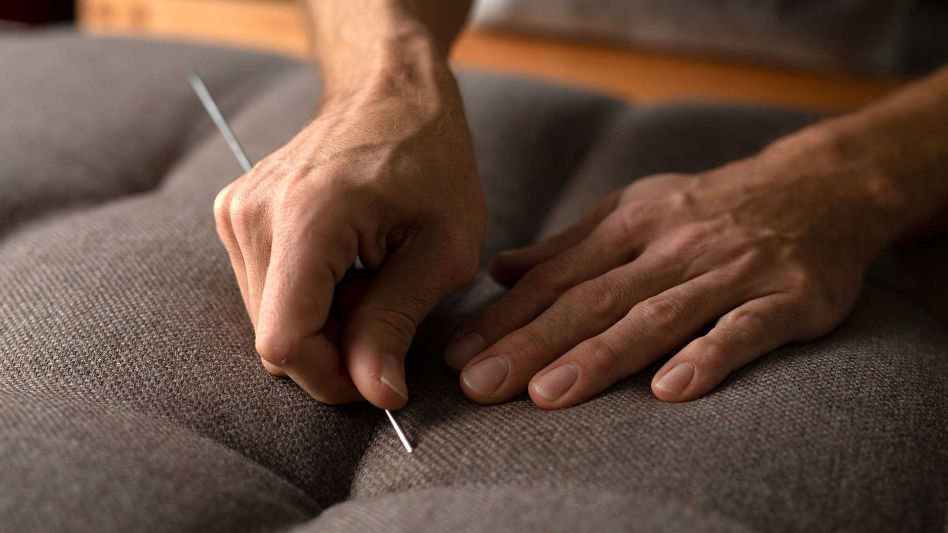 Nahaufnahme zweier Hände, die eine handwerkliche Tätigkeit an einem Polstermöbelstück oder einer Matratze ausführen