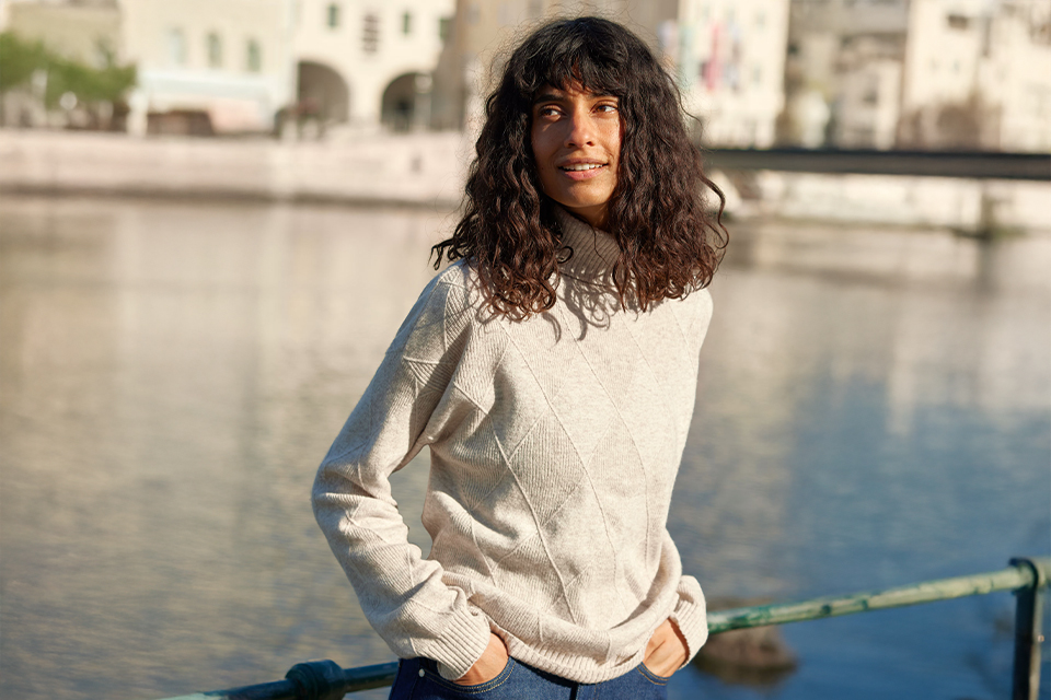 Frau in heller Kleidung steht am Wasser in Stadtnähe