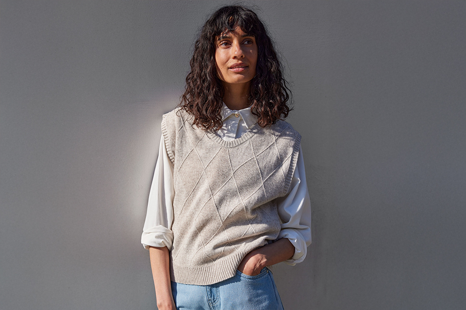 Frau trägt hellen Pullover vor neutralem Hintergrund