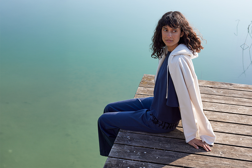 Frau sitzt entspannt auf Steg am ruhigen Seeufer