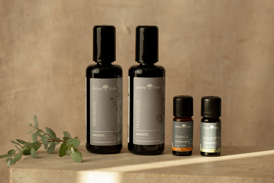 Zwei Basisöle und zwei Aromaöle neben einem dekorativen Zweig