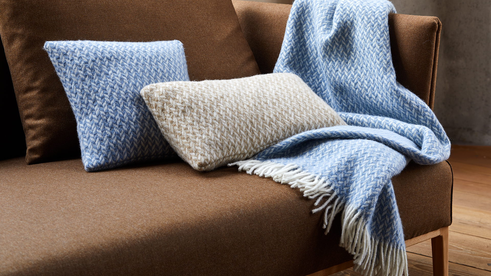 Zierkissen und Wohndecke auf einem braunen Sofa liegend