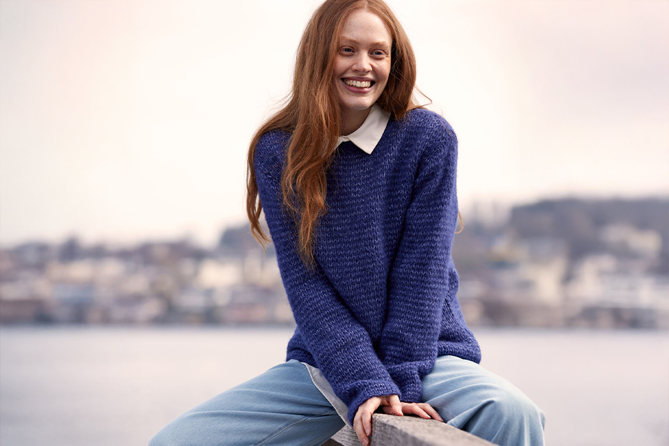 Lächelnde Frau im blauen Pullover mit unscharfem Hintergrund