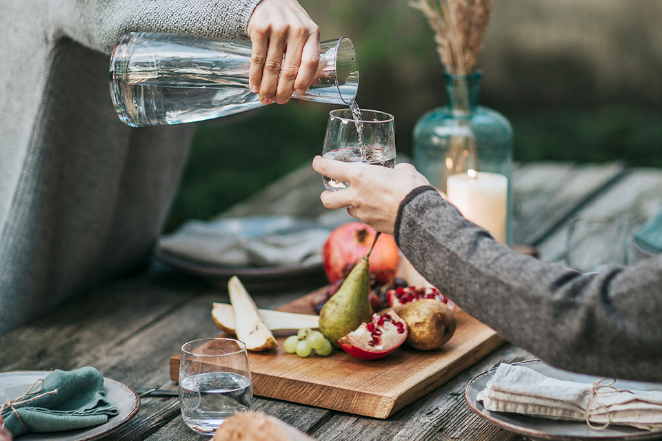 Über einem gedeckten Tisch wird mit einer Glaskaraffe Wasser eingeschenkt