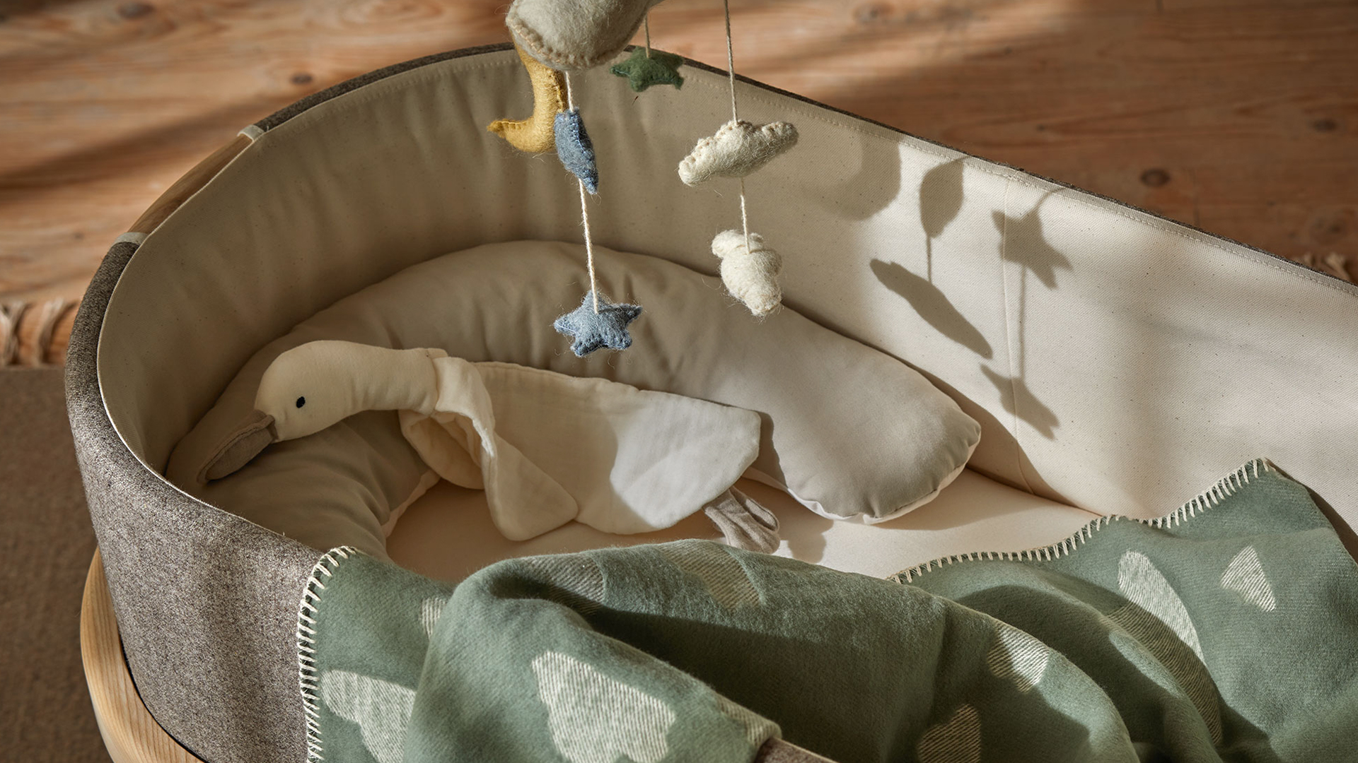 Graue Babywiege mit Kuschelgans und einer Kuscheldecke mit Wolkenmuster