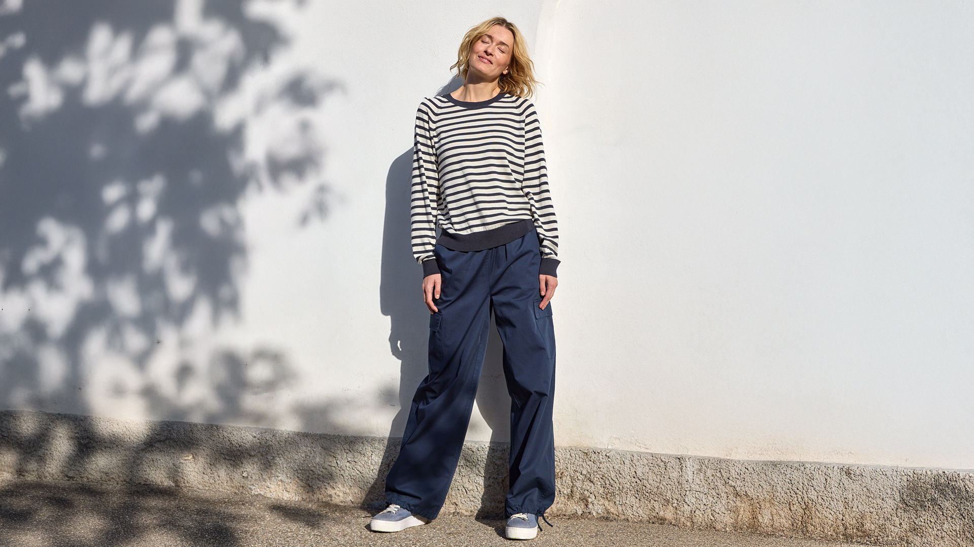 Person steht draußen im Sonnenlicht vor einer Wand