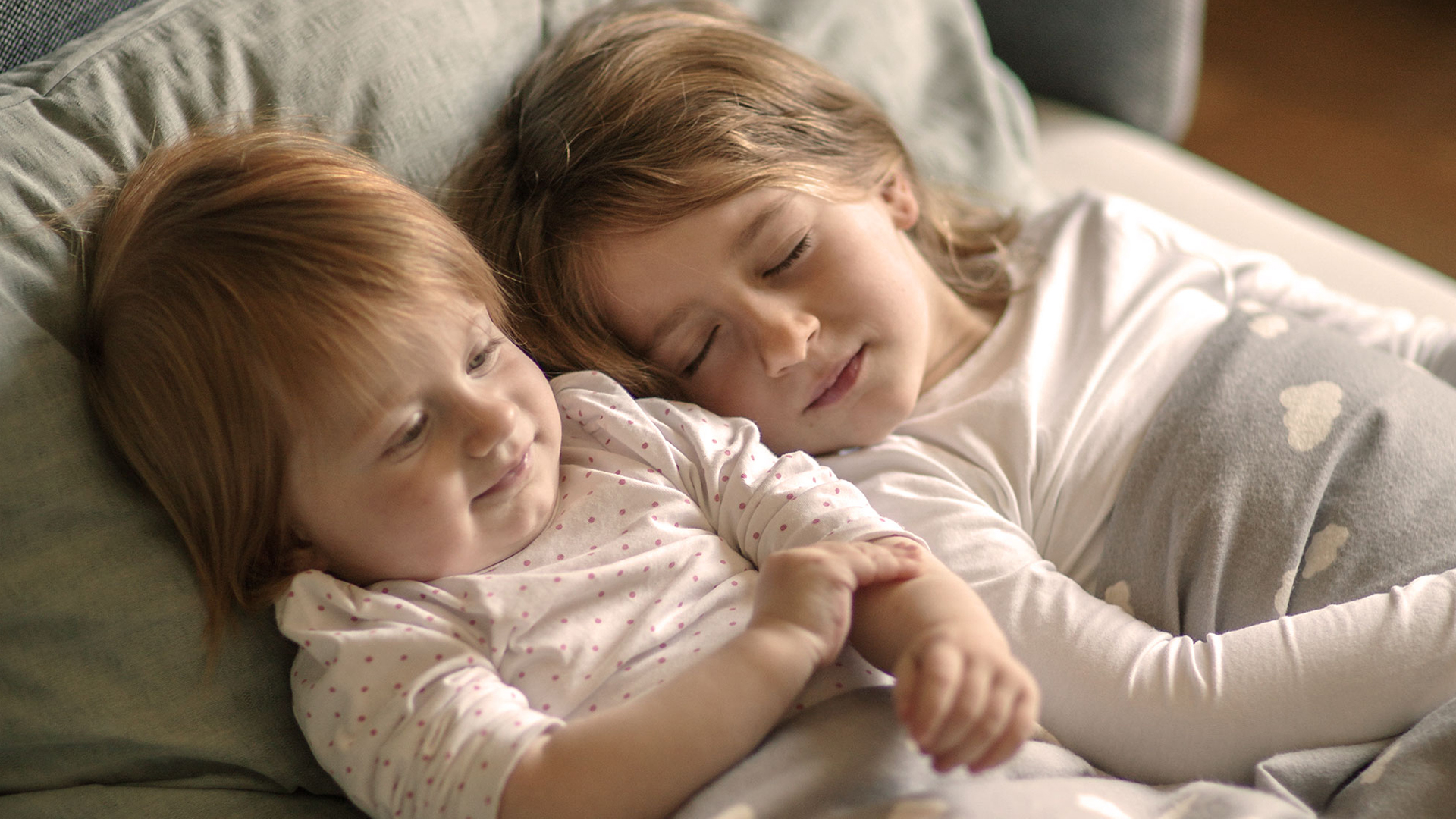 Zwei kleine Kinder in einem Bett liegend aneinandergekuschelt