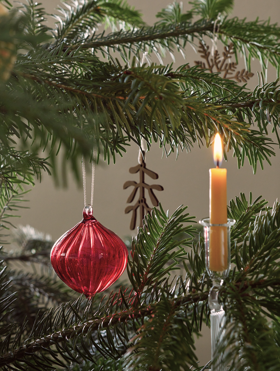 Rote Weihnachtskugel und gelbe Kerze hängen am Christbaum