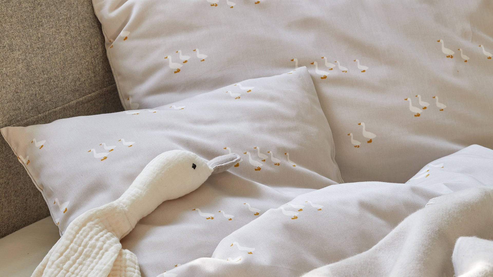 Graue Bettwäsche mit Gänsedesign und Kuschelgans auf dem Bett liegend