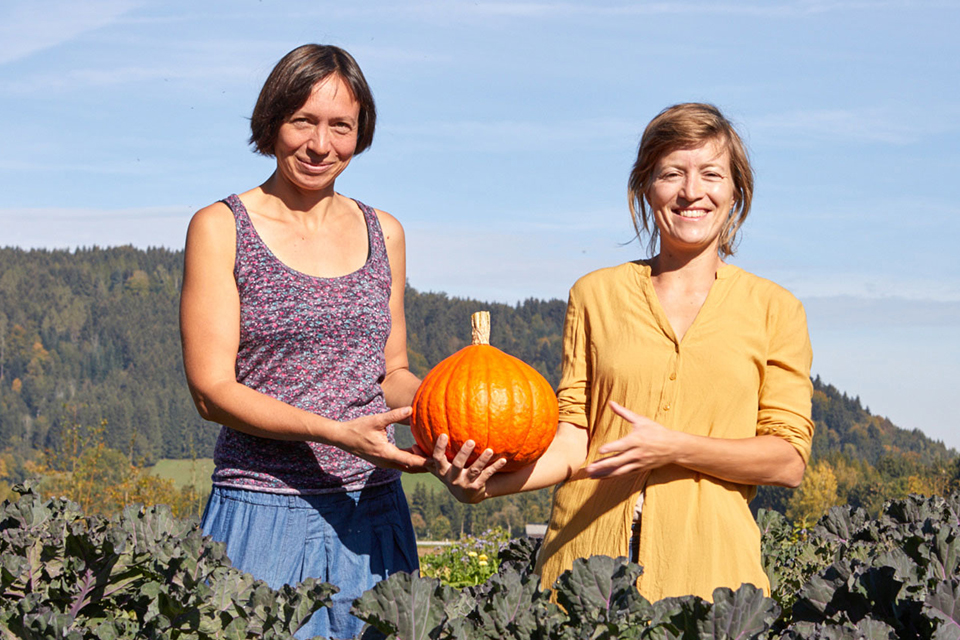 Zwei Frauen auf einem Feld halten gemeinsam einen Kürbis in ländlicher Umgebung
