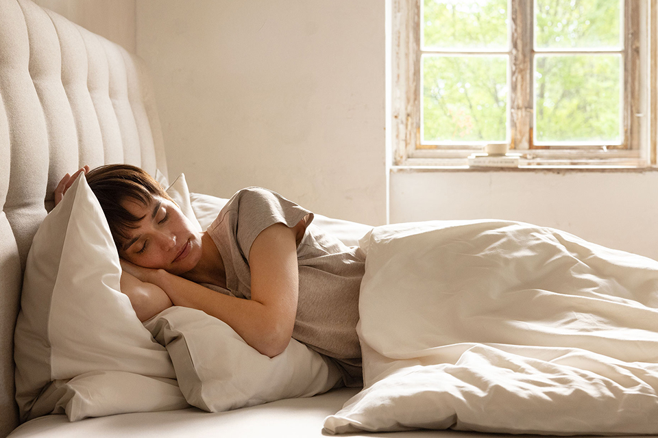 Eine Frau schläft in einem Bett mit Betthaupt und heller Bettwäsche