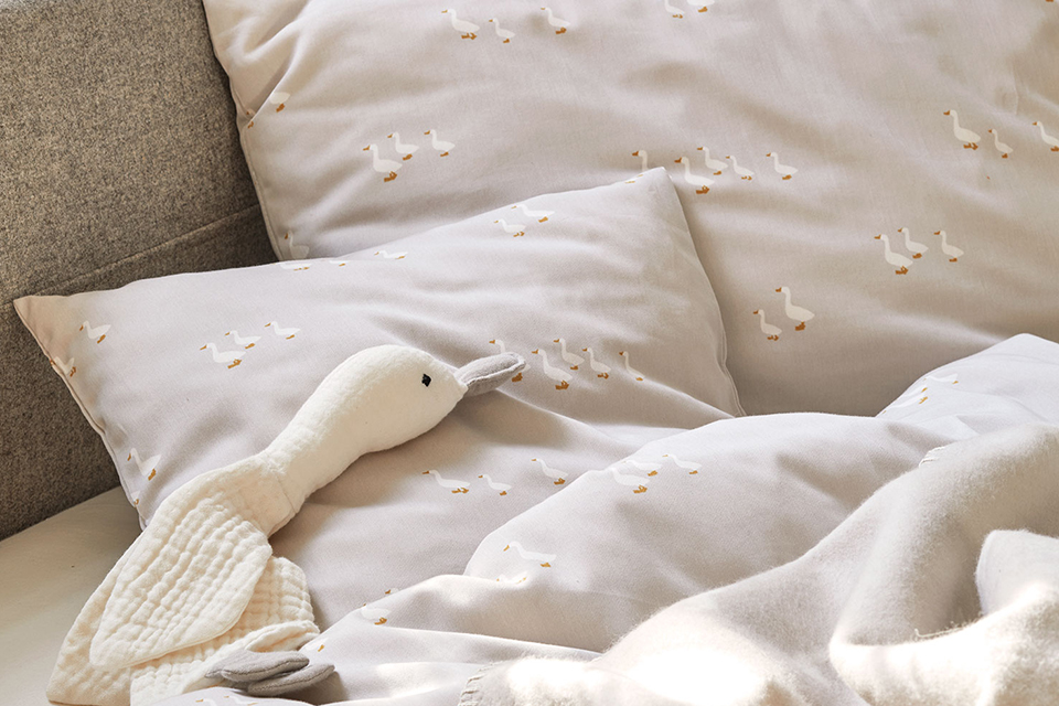 Graue Bettwäsche mit Gänsedesign und Kuschelgans auf dem Bett liegend