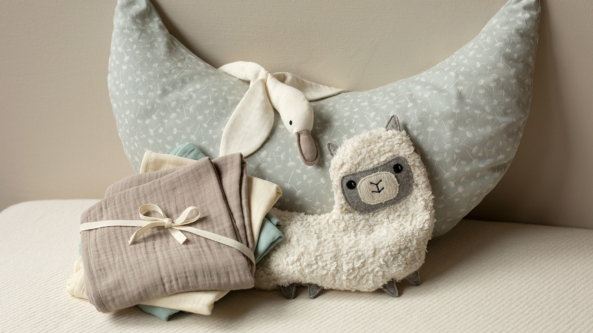 Halbmondkissen mit Kuscheltieren und Stoffwindetset aneinander arrangiert