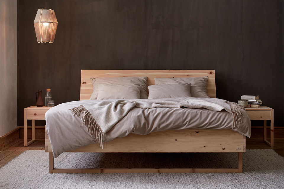 Zirbenbett Akato vor einer dunkelbraunen Wand