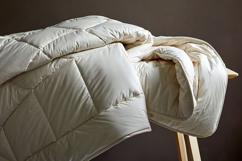 Drei Bettdecken liegen gefaltet auf einer Holzbank