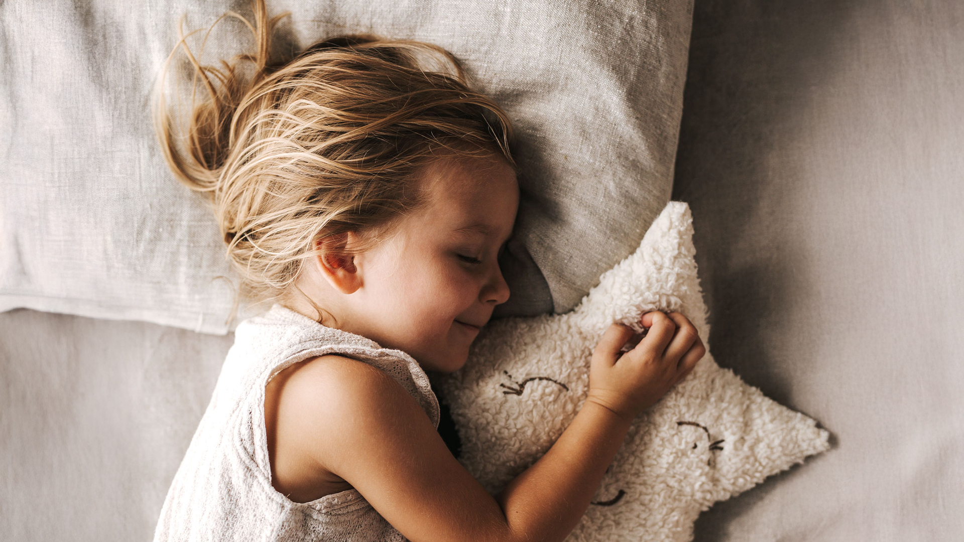 Kind schläft imBett mit einem Kuscheltier in der Hand
