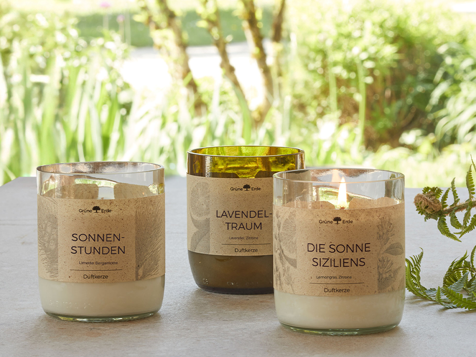 Drei Duftkerzen in natürlicher Umgebung mit dekorativem Zweig