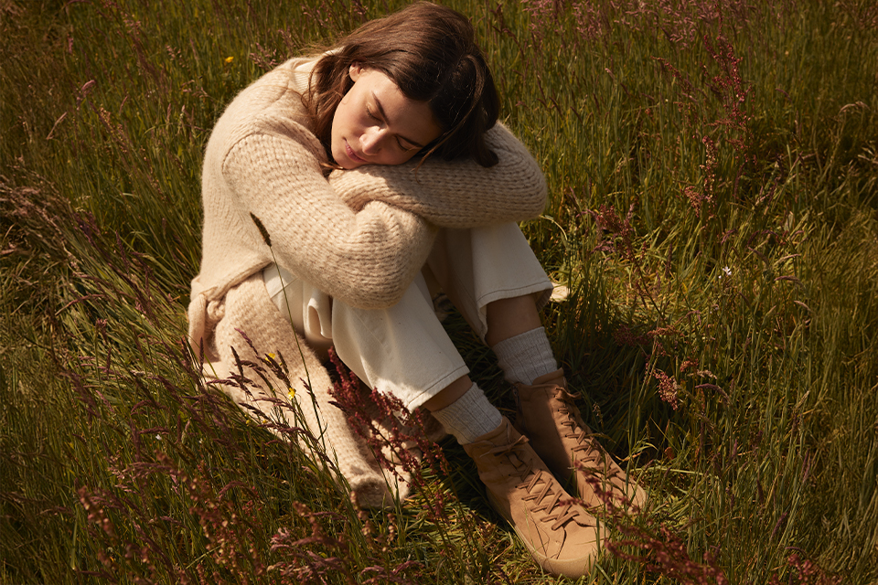 Person sitzt eingekuschelt im Gras mit warmer Kleidung