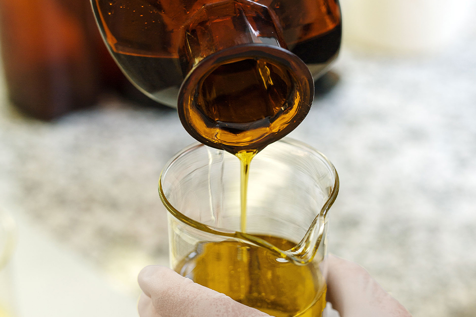 Öl wird aus Glasflasche in einen Messbehälter gegeossen