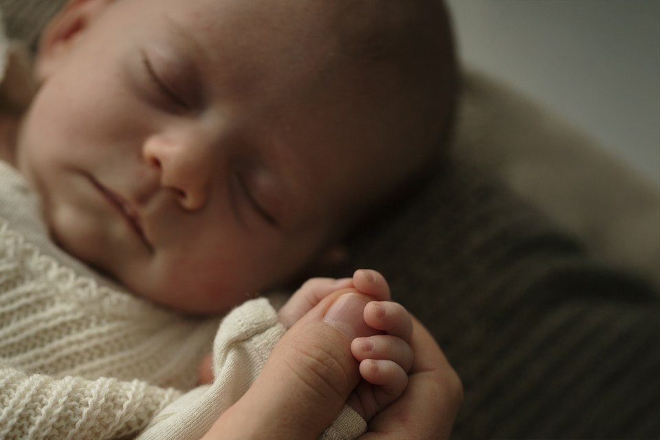 Schlafendes Baby hält den Daumen der Mutter fest