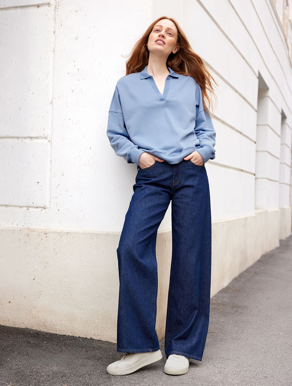 Frau trägt hellblauen Pullover mit Kragen und dunkelblaue Jeans mit weißen Turnschuhen