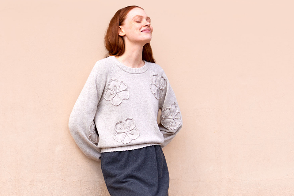 Frau im grauen Sweatshirt vor schlichter beiger Wand