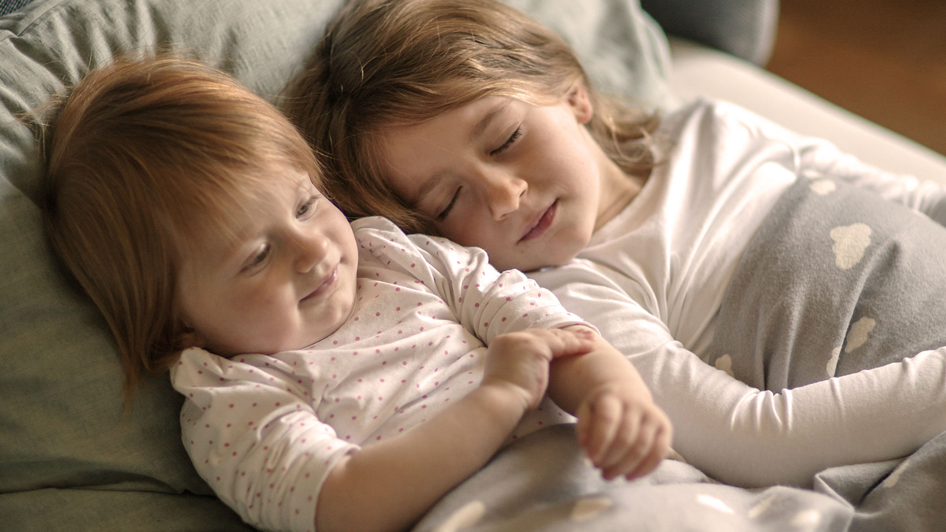 Zwei kleine Kinder in einem Bett liegend aneinandergekuschelt