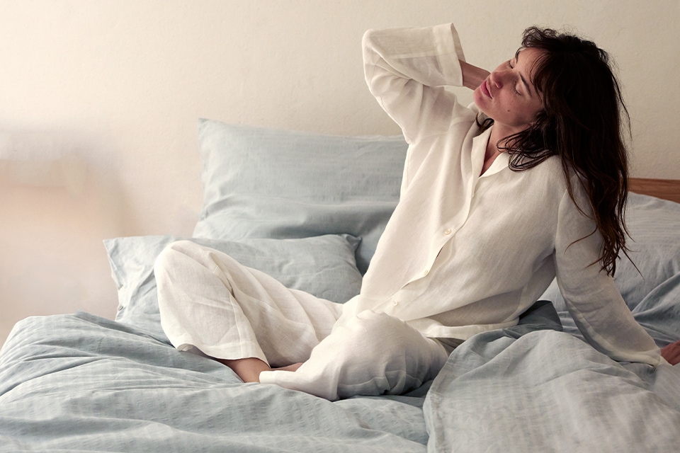 Frau mit hochwertigem weißen Pyjama in einem Bett mit Bettwäsche Orlando in blaugrau