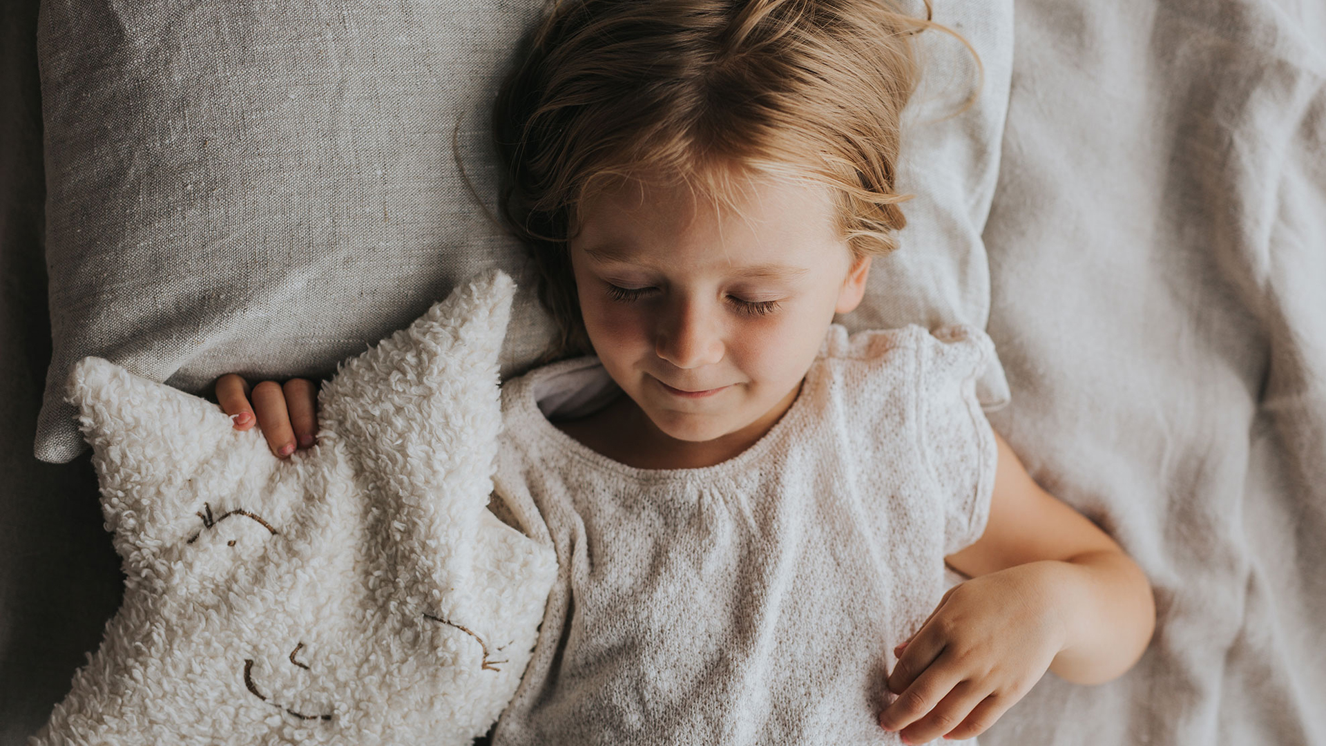 Kind liegt im Bett mit Kuschelkissen