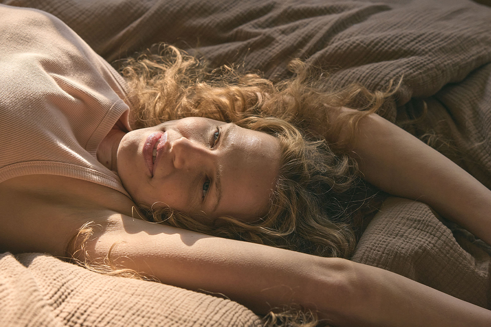 Blonde Frau liegt in einem Bett mit der Bettwäsche Vivien in der Farbe nougat
