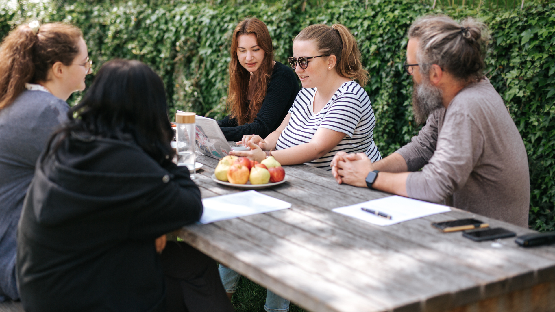 Teammeeting im Freien mit mehreren Personen am Tisch
