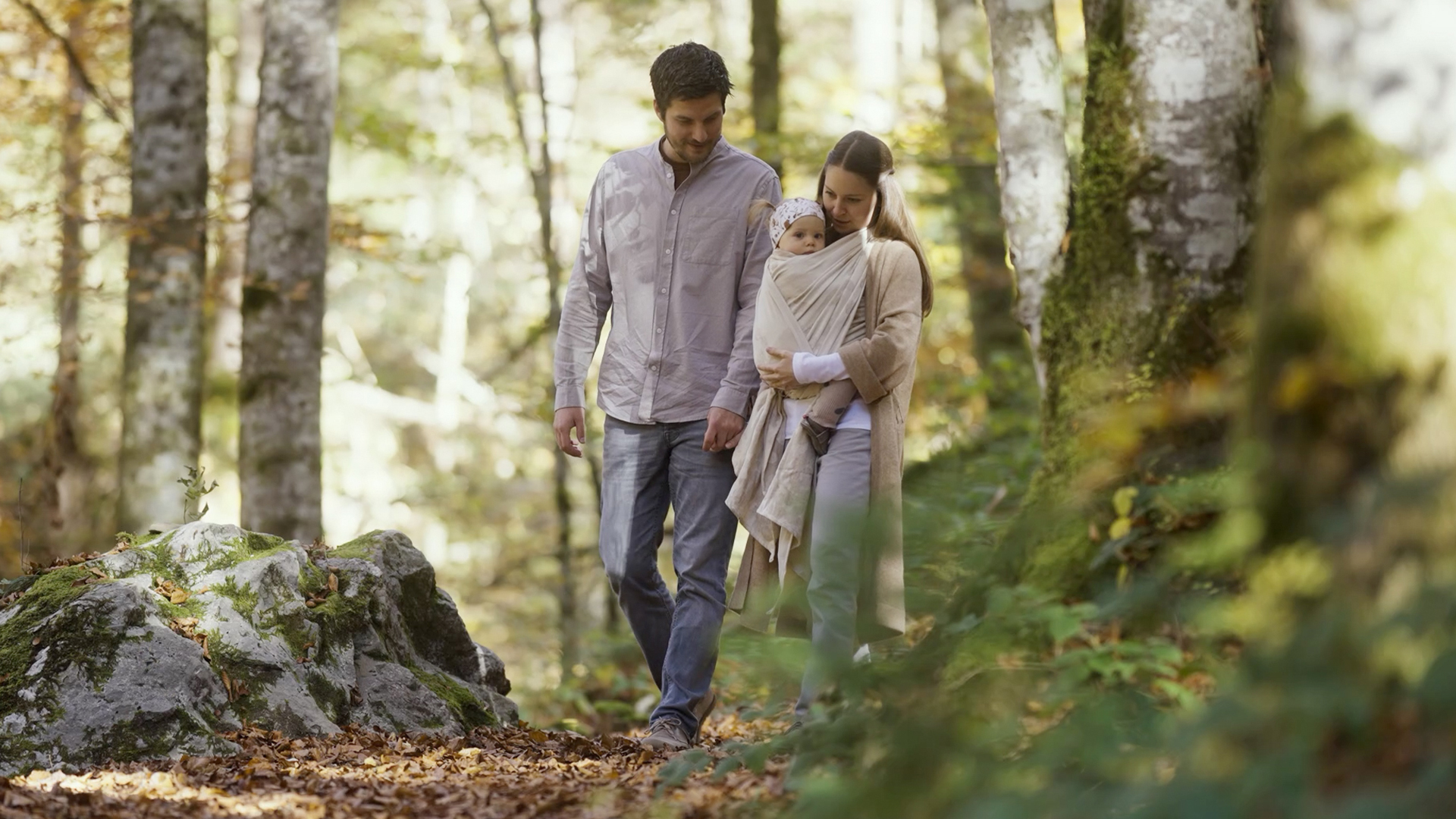 Mutter und Vater gehen mit Kind im Tragetuch im Wald spazieren