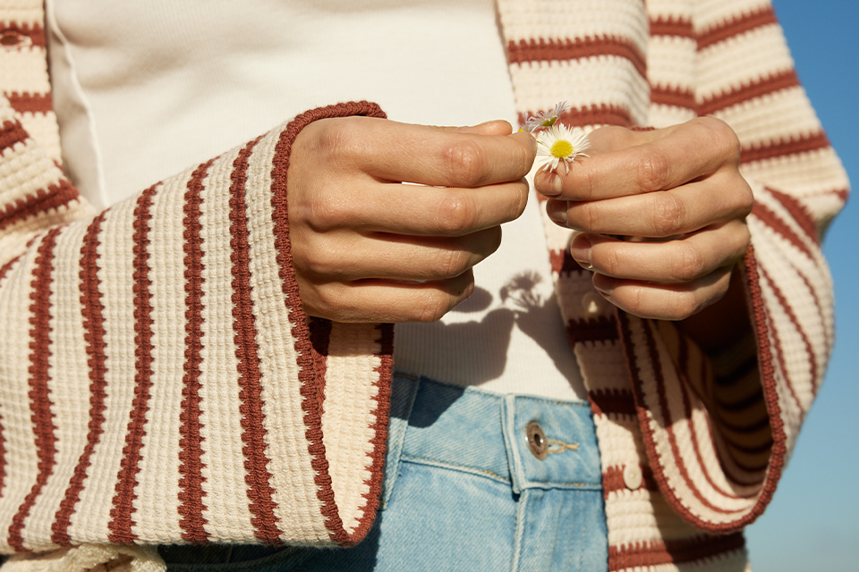 Person im gestreiften Sweater hält ein kleines Gänseblümchen in der Hand