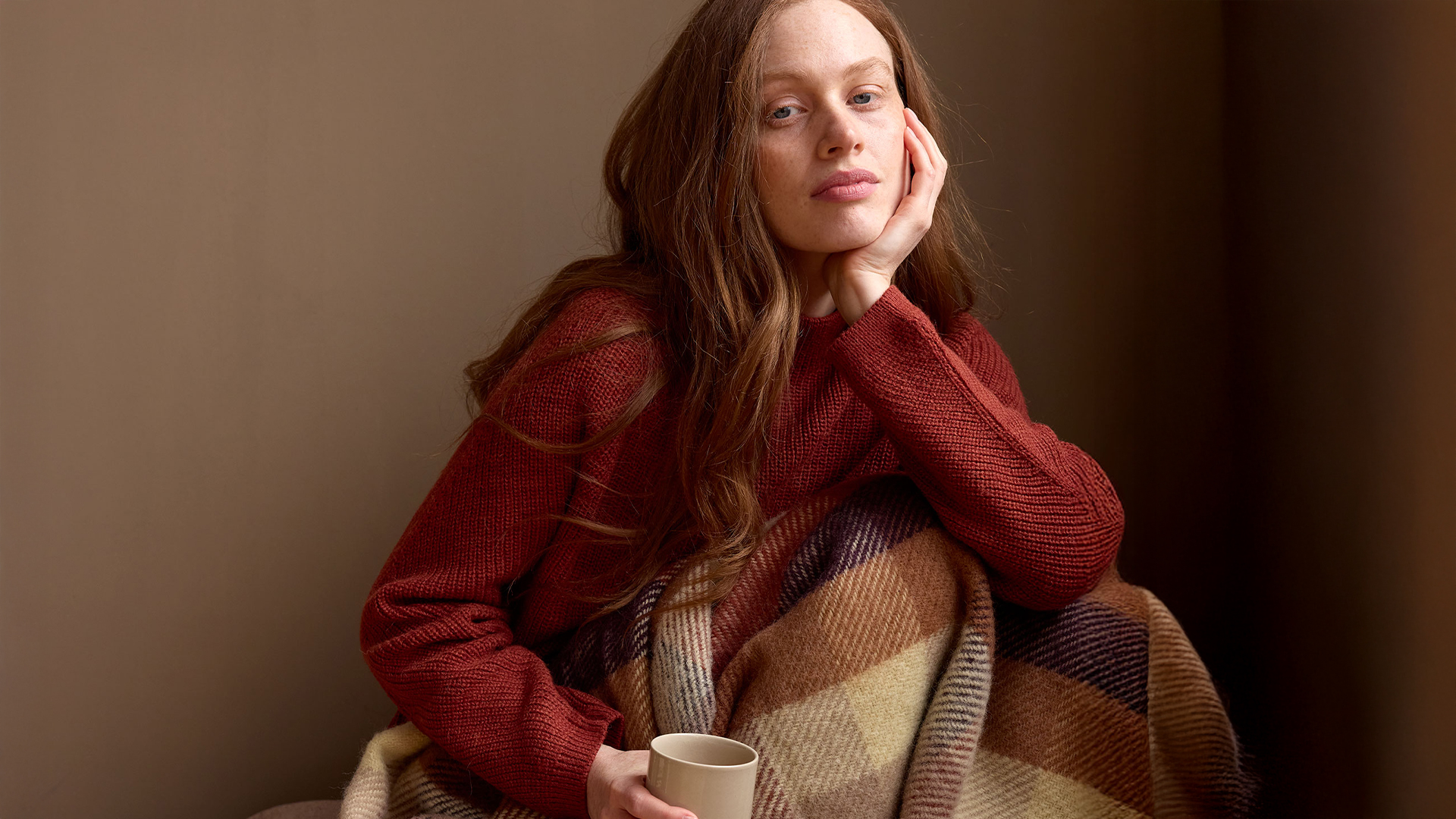 Frau in rotem Outfit sitzt gemütlich mit Decke im warmen Licht