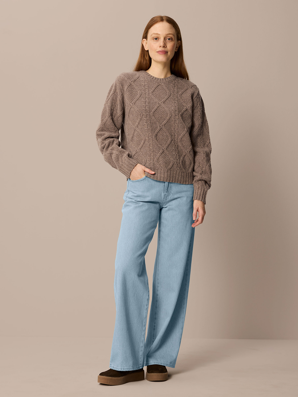 Frau trägt braunen Pullover und eine hellblaue Jeans