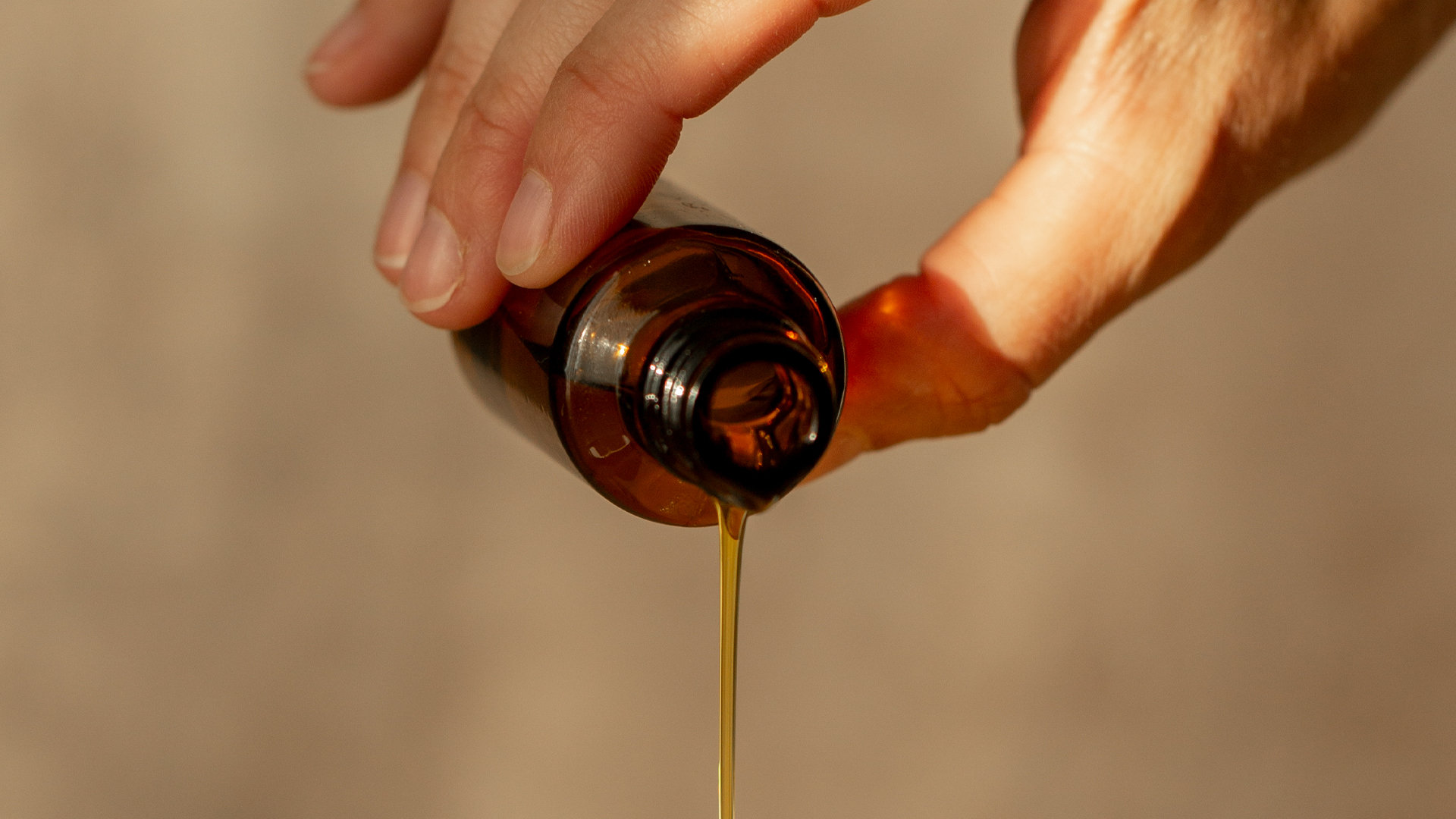 Hand hält Behälter aus dem Öl fließt