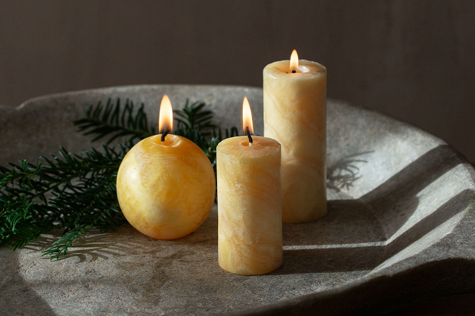 Kerzen aus Bienenwachs in einer Keramikschale und einem Tannenzweig