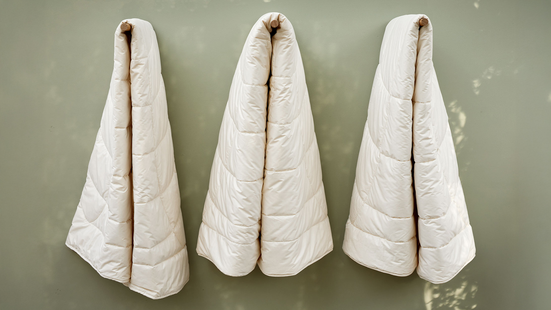 Drei Schlafdecken hängen an Holzstangen vor einer grünen Wand