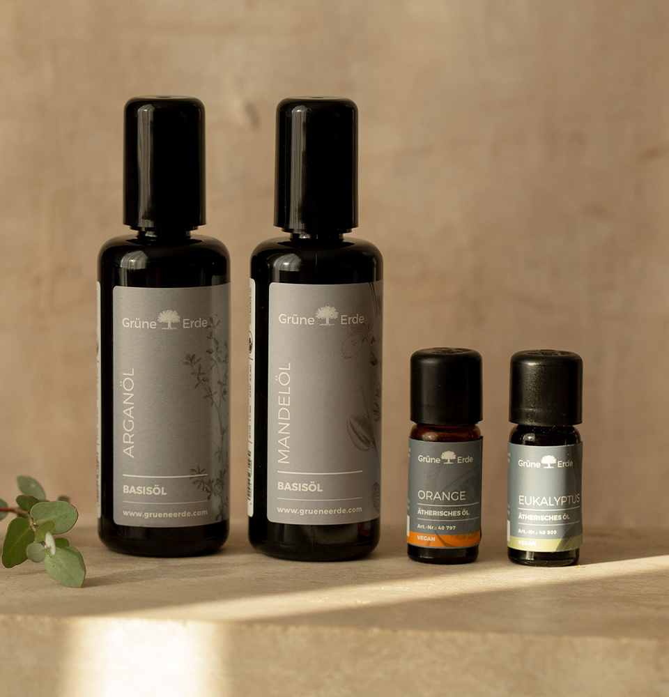 Zwei Basisöle und zwei ätherische Öle stehen auf Steinplatte mit dekorativem Zweig