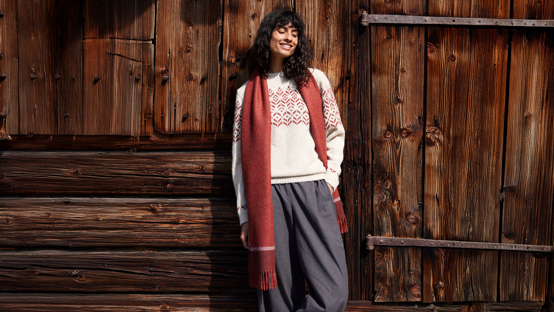 Frau in Mantel steht vor rustikaler Holzfassade