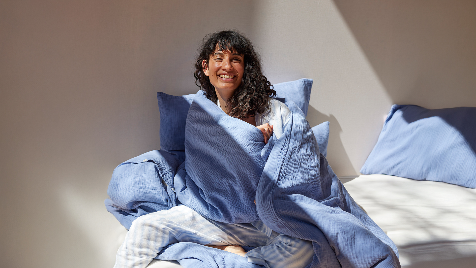 Frau mit blau weiß gestreiftem Pyjama in einem Bett mit blauer und weißer Bettwäsche