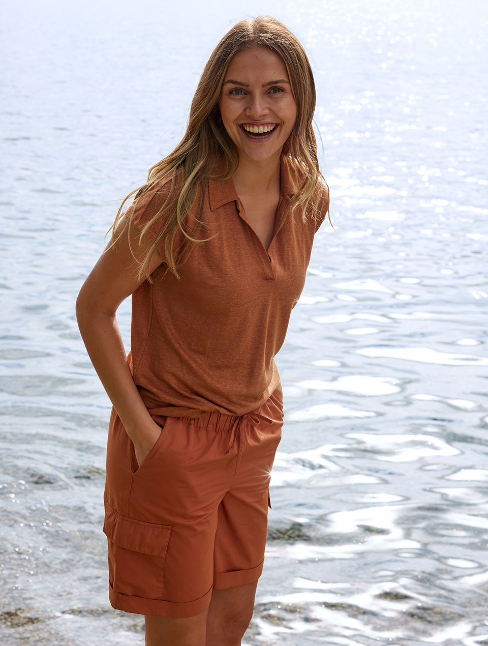 Frau in orangem Shirt und kurzer oranger Cargohose vor einem See