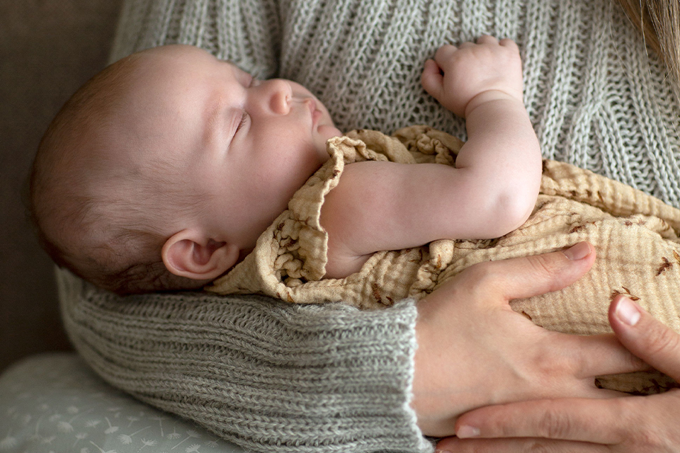 Schlafendes Baby im Arm der Mutter liegend
