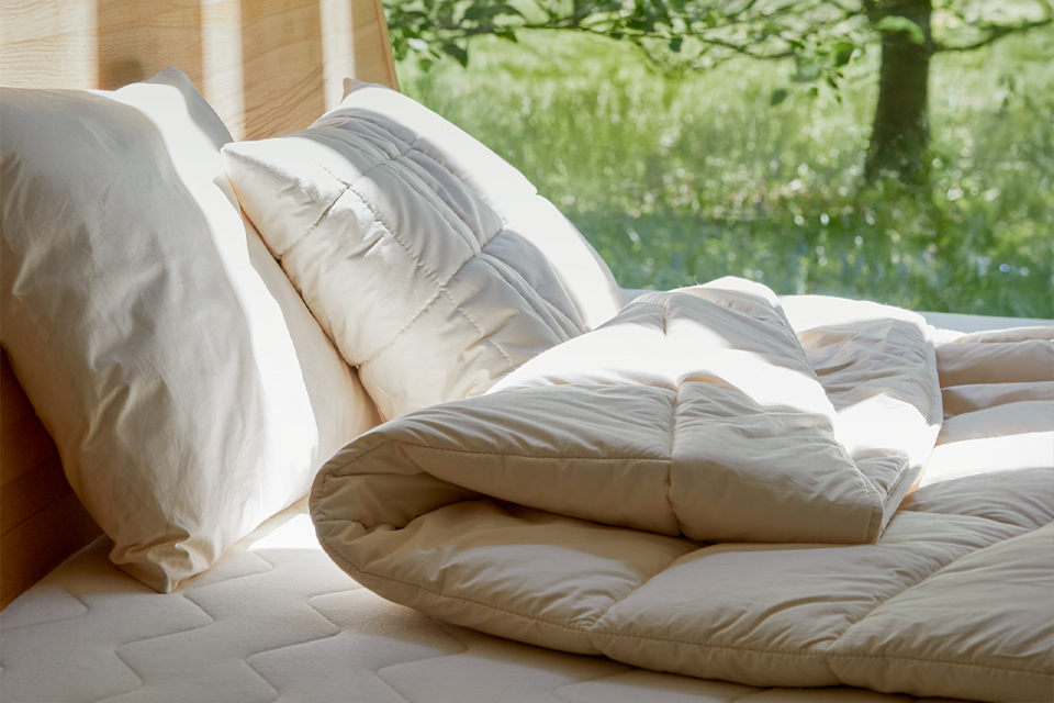 Schlafkissen und Bettdecke in Vollholzbett auf einer Wiese mit einem Baum